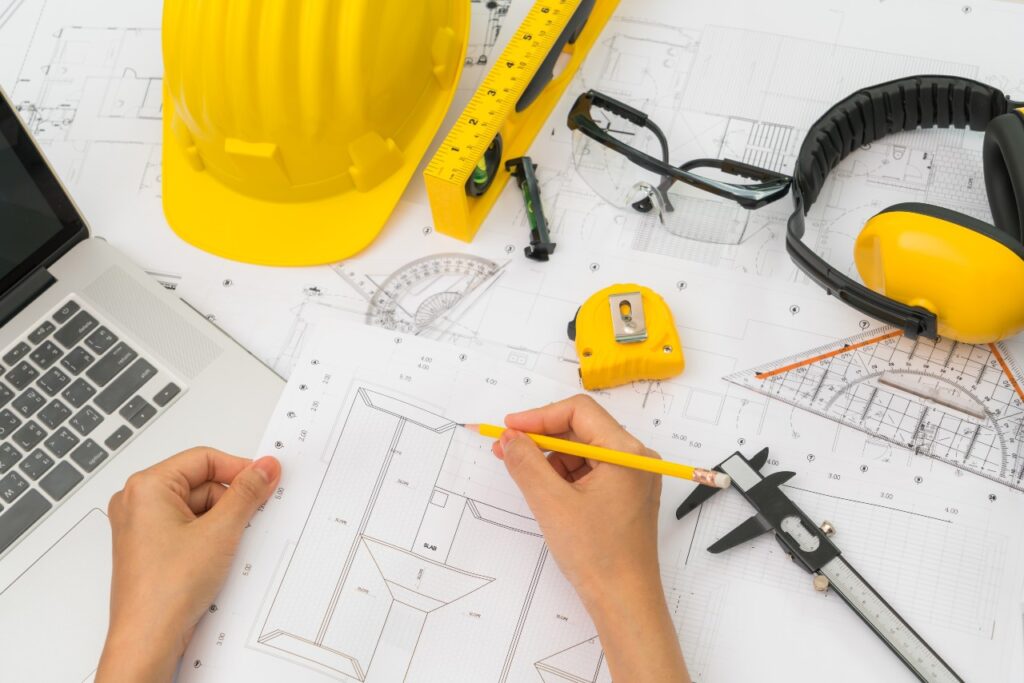 hand-over-construction-plans-with-yellow-helmet-and-drawing-tool